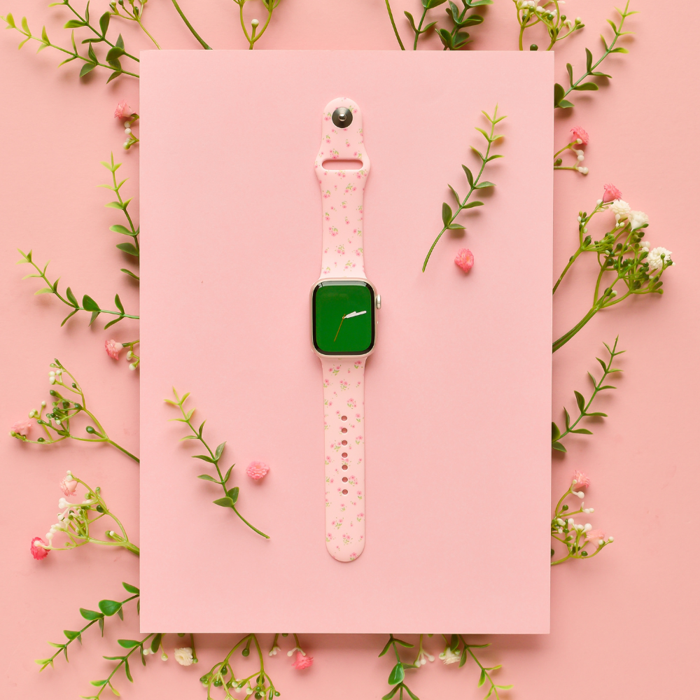 Pink Apple Watch strap with a ditsy floral pattern, displayed on a pink background with small flowers and green sprigs.