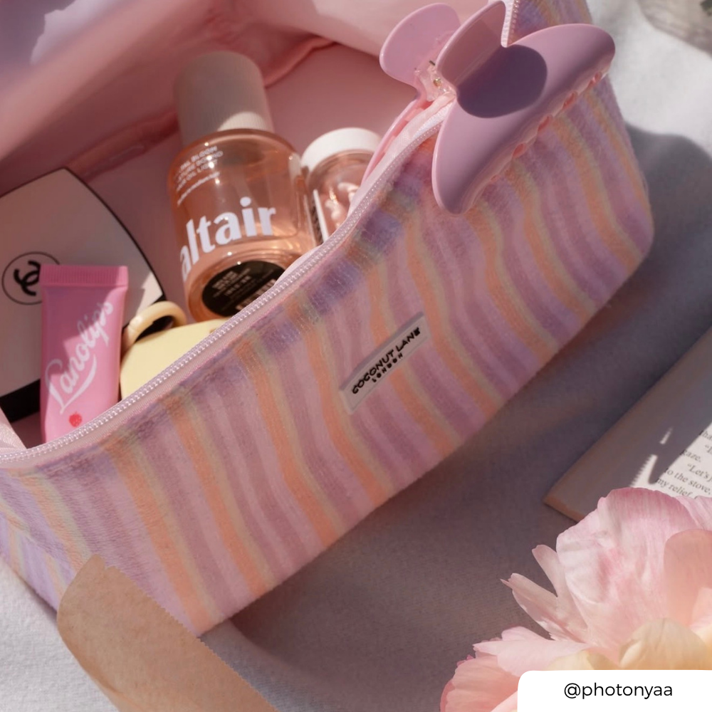 Pink striped makeup bag with cosmetic items and a flower on a light background