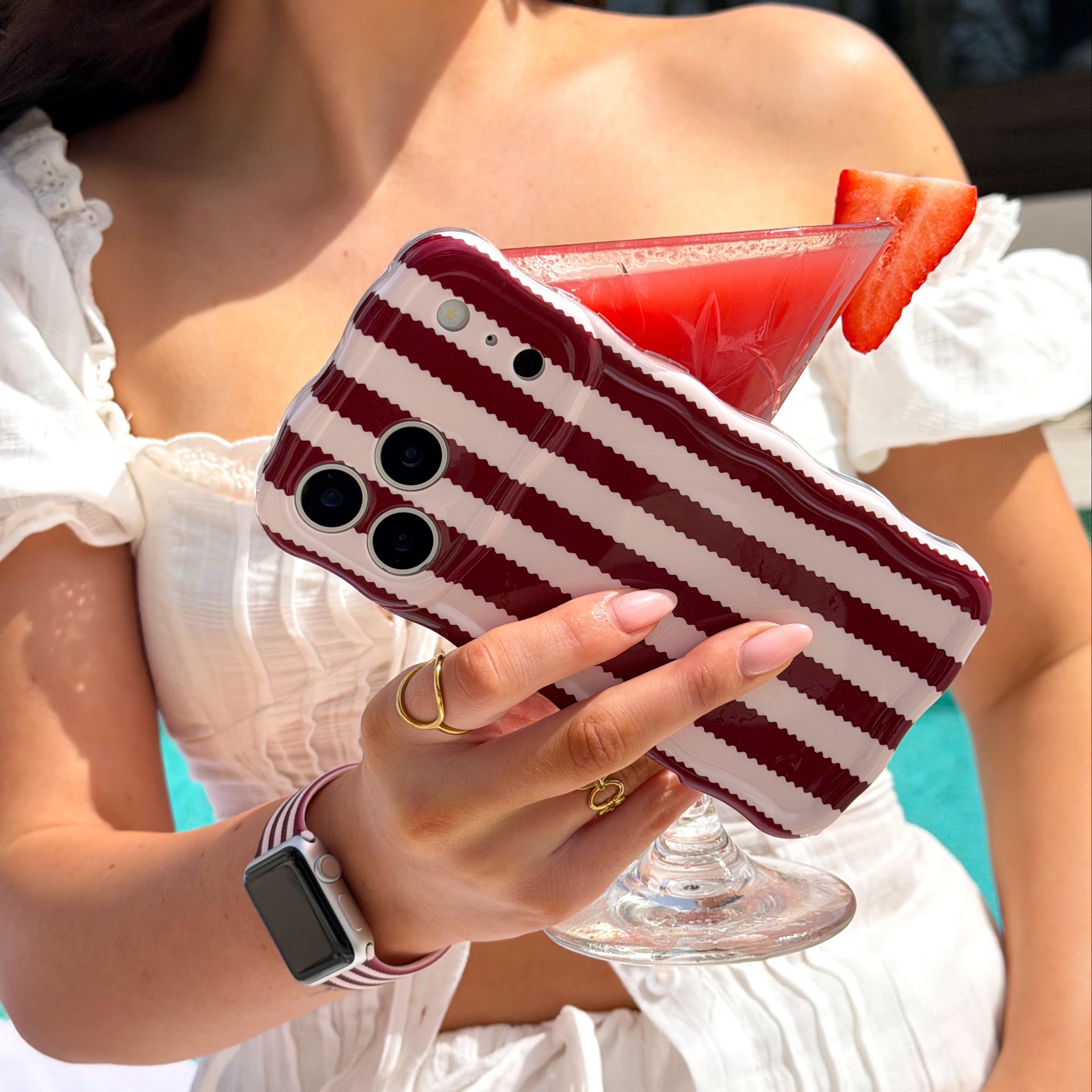 Girl holding a phone with Blushberry stripes case, and strawberry daiquiri.