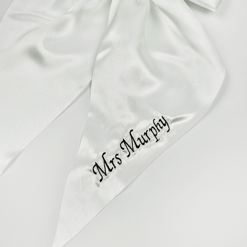 A white satin ribbon with the words "Mrs Murphy" embroidered in black script on one of its pointed ends.