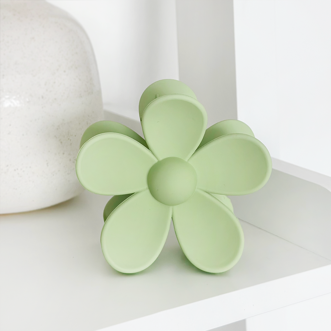 A decorative item shaped like a green flower with six petals is placed on a white shelf next to a white, speckled vase.