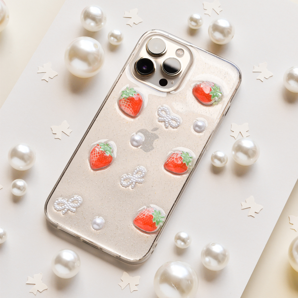 A smartphone with a peach-colored case featuring a cute teddy bear pattern lies on a peach and brown background, surrounded by paper cutouts shaped like bear heads.