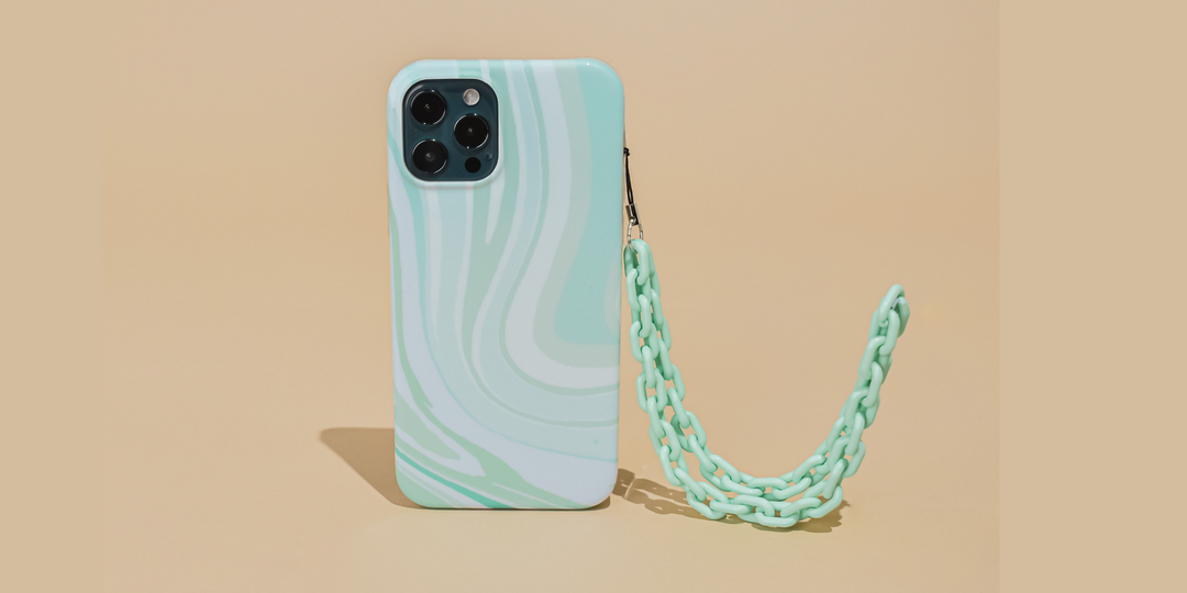 A mint green and white marble-patterned phone case with a matching plastic chain is displayed upright against a beige background. The case features four camera cutouts.