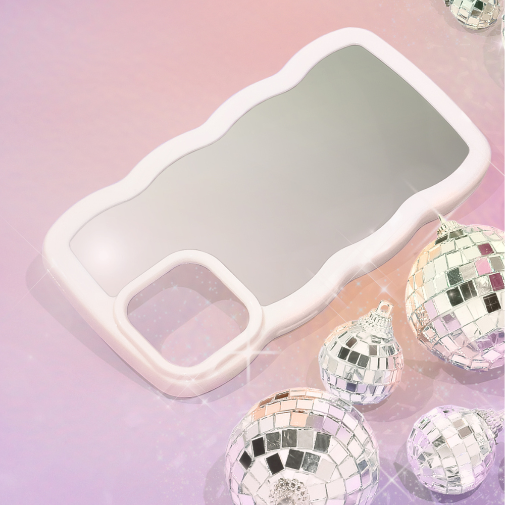 A sleek and stylish Curvy Mirror Phone Case - Cream from Coconut Lane lies on a pink and purple gradient background. Surrounding the curvy mirror phone case are several shiny, mirrored disco ball ornaments of varying sizes, reflecting light and casting a festive, glamorous feel to the image.