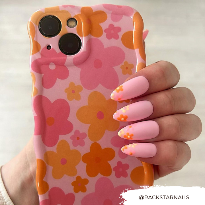 A hand with pastel pink nails featuring orange floral designs holds a Coconut Lane Wavy Phone Case - Pink & Orange Bloom. The user's handle @RACKSTARNails is displayed in the bottom right corner.