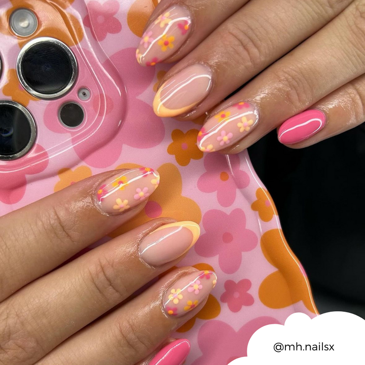 A close-up of hands with manicured nails featuring a vibrant design. The nails showcase pink and orange flower patterns along with yellow French tips. The Wavy Phone Case - Pink & Orange Bloom by Coconut Lane, held in one hand, complements the nail art perfectly with its matching floral design. Image credit: @mh.nailsx.