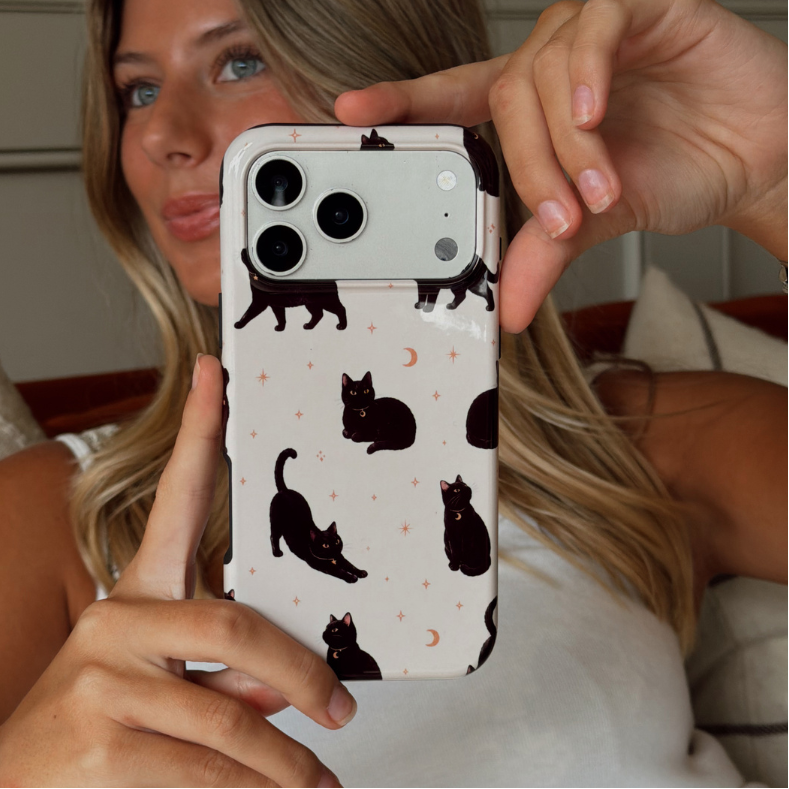 Woman holding up an iphone, showing a phone case with black cats printed on the case.