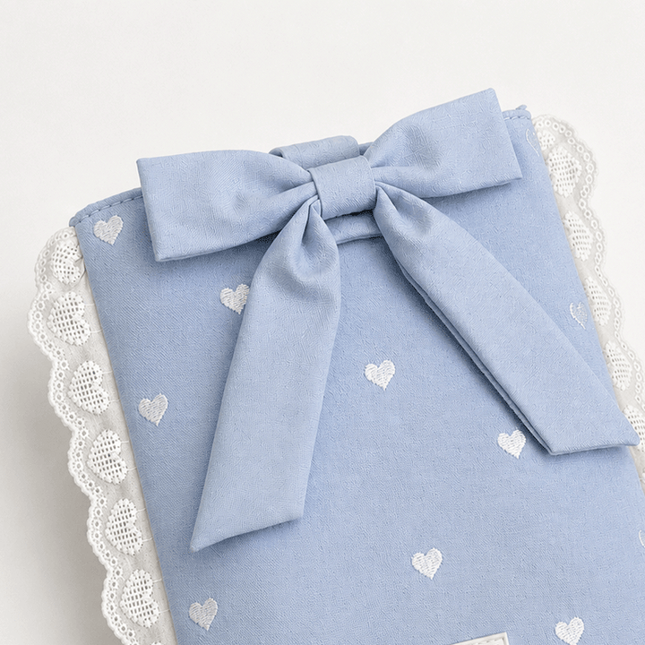 Blue fabric Book Sleeve with embroidered heart design, bow closure and white lace edging.