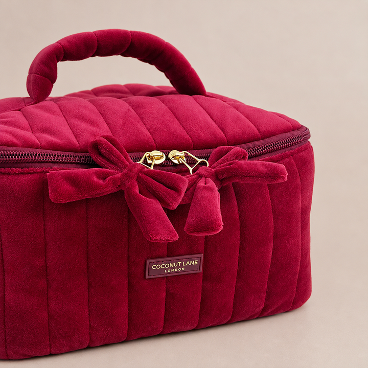 Burgundy velvet cosmetic bag with a quilted design, top handle, bow detail, and gold-tone hardware.