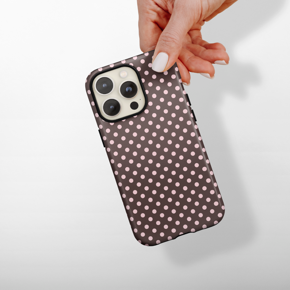 Hand holding a dual-layer phone case with brown polka dots and pink spots on a white background.