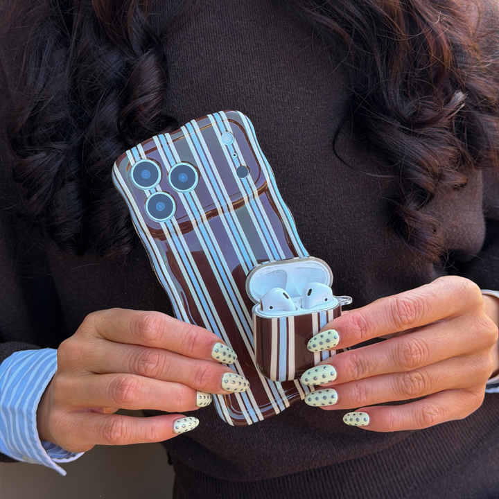 Girl holding Brown and Blue Stripe AirPods Case next to matching wavy phone case