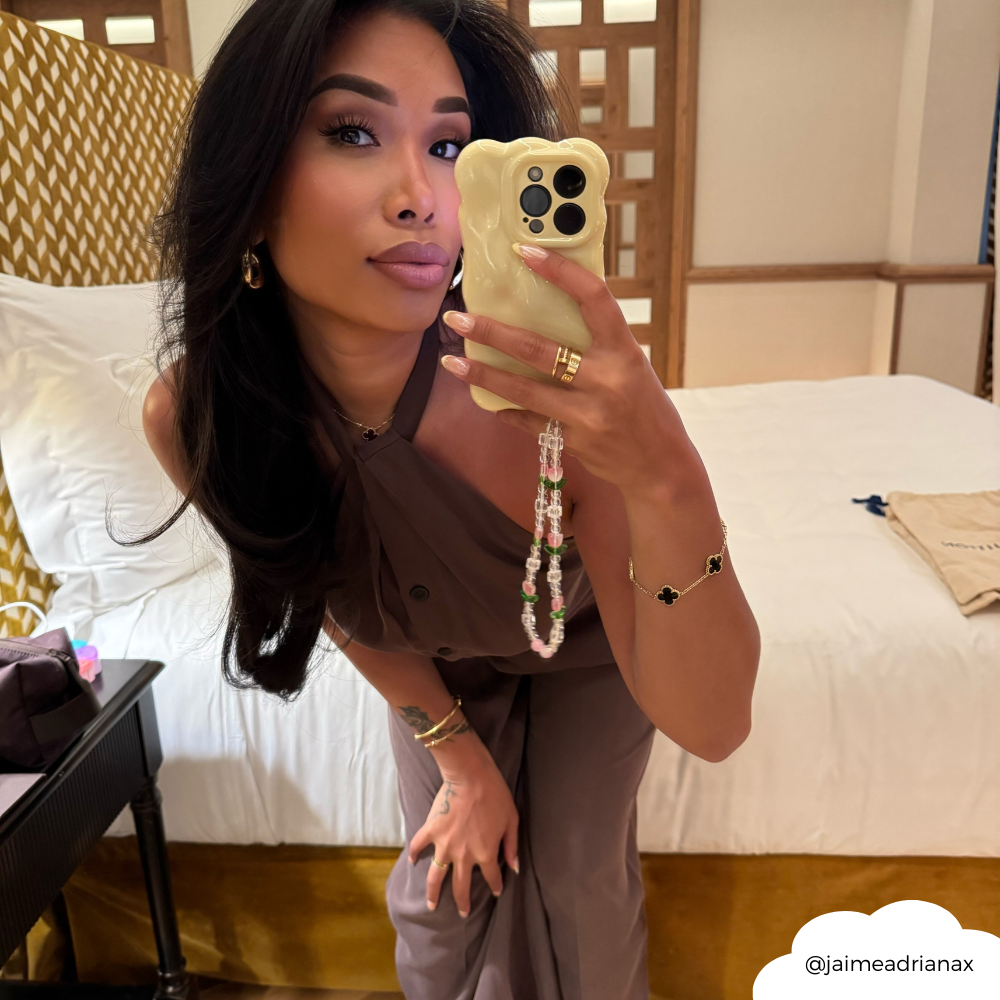 Woman in a brown outfit takes a mirror selfie holding a butter yellow 3D bubble phone case with a floral beaded strap.