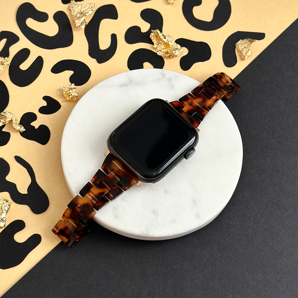 Slim tortoiseshell Apple Watch strap by Coconut Lane on a white tray with gold flecks and a leopard-print background.