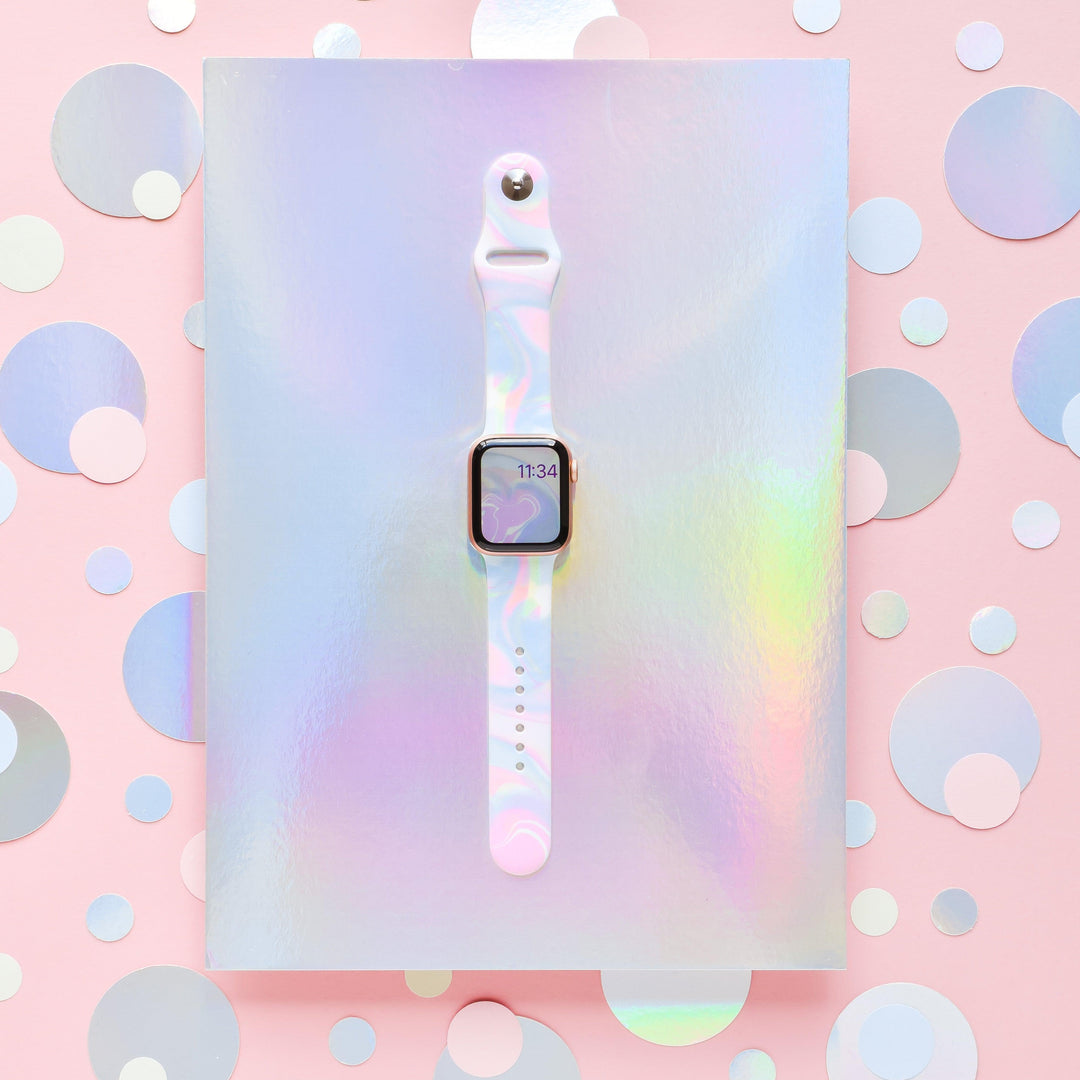 A Coconut Lane smartwatch featuring the Holo Bubble Apple Watch Strap is showcased against a holographic background. The smartwatch screen displays the time as 11:34. The scene is vibrant, with a pastel color scheme and variously sized shimmering dots on a pink backdrop, highlighting its iridescent holographic design.