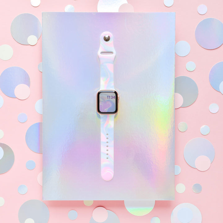 A Coconut Lane smartwatch featuring the Holo Bubble Apple Watch Strap is showcased against a holographic background. The smartwatch screen displays the time as 11:34. The scene is vibrant, with a pastel color scheme and variously sized shimmering dots on a pink backdrop, highlighting its iridescent holographic design.