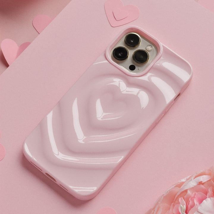 A Coconut Lane Melting Heart Phone Case in Peony Pink encases a smartphone resting on a pink surface. Multiple paper hearts are scattered around, enhancing the romantic and playful theme. The background features an array of pink shades and textures.