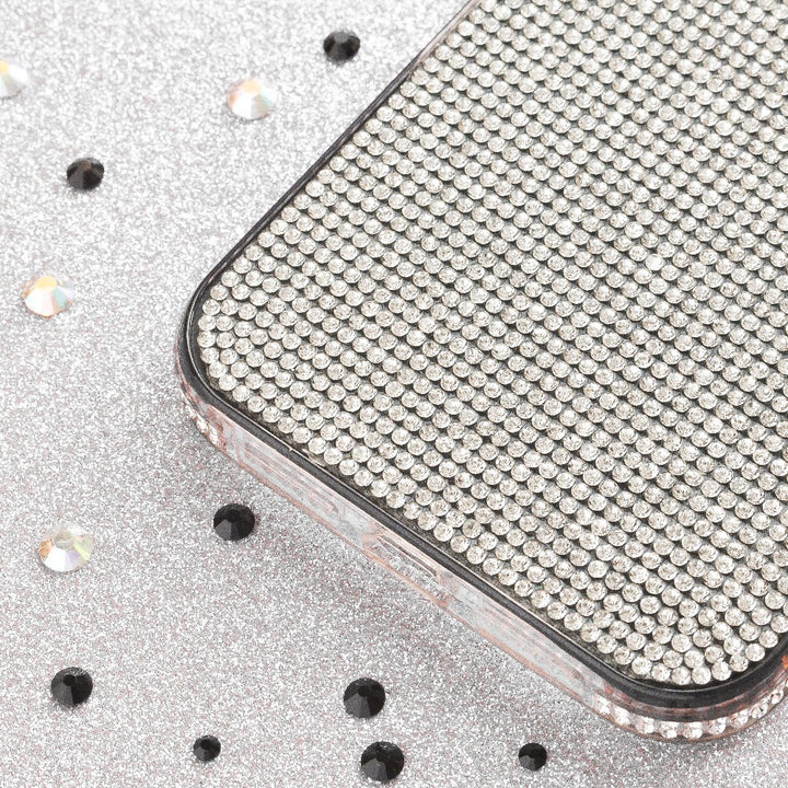 A close-up of the Coconut Lane Disco Sparkle Phone Case - Silver, adorned with countless tiny, sparkling rhinestones. The background shimmers on a glittery silver surface dotted with black specks and small rhinestones, enhancing the scene's overall sparkle and shine.