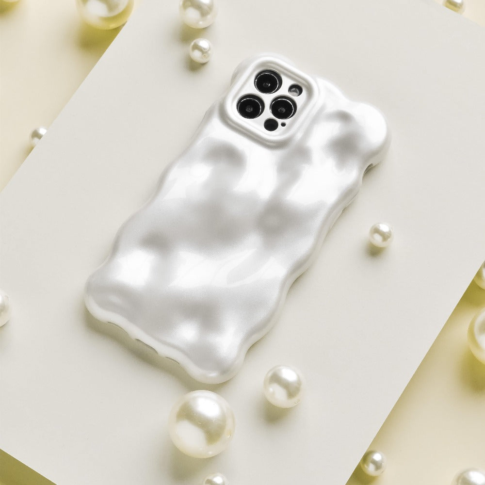 An iPhone with a glossy, ripple-patterned white case is displayed on a white rectangular surface. Surrounding the phone are scattered white pearls and Coconut Lane's 3D Pearl Phone Case - White, adding a touch of elegance to the composition.