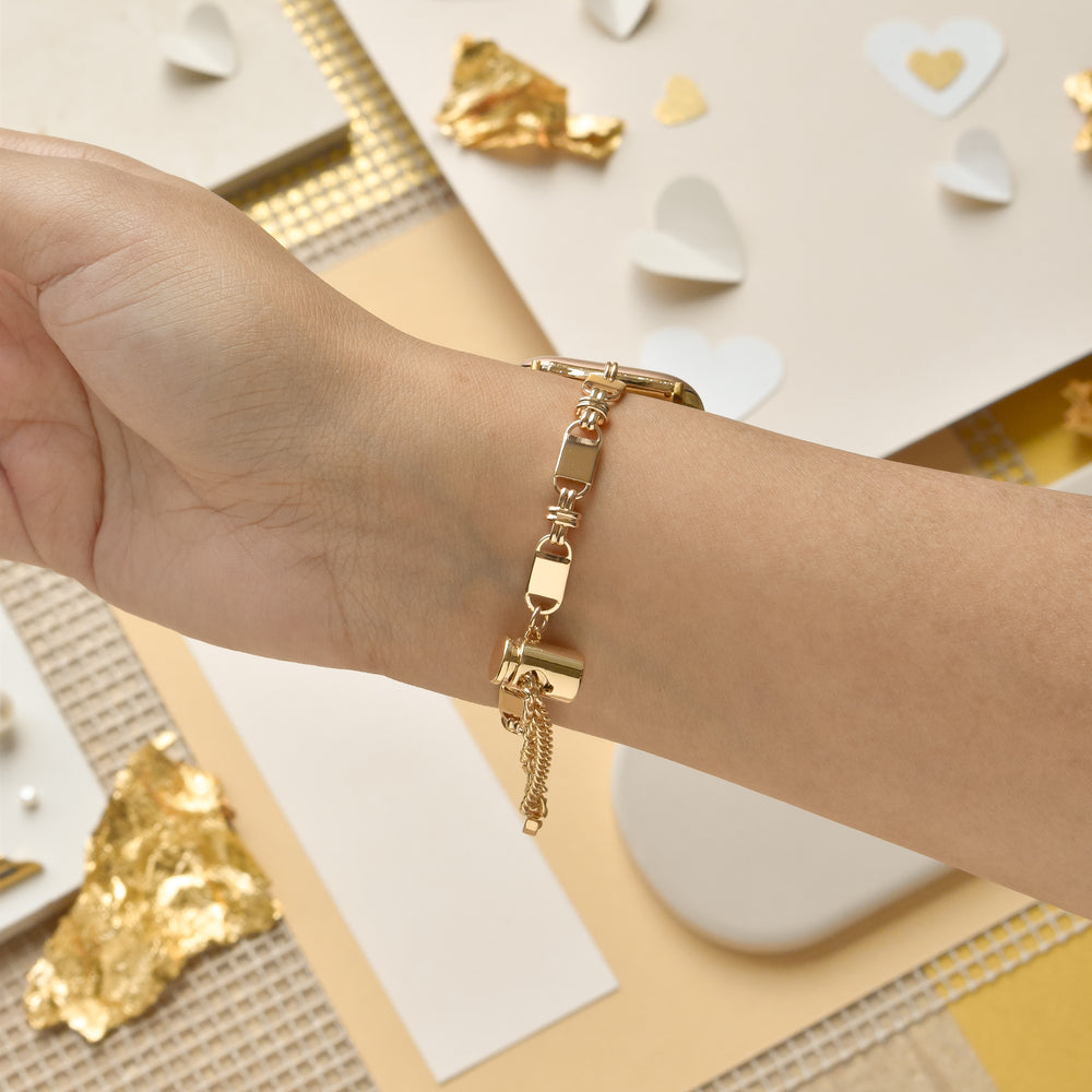 A close-up of a wrist adorned with Coconut Lane's Simple Gold Bracelet Apple Watch Strap featuring geometric links. The background showcases a soft, warm-toned setup with scattered paper hearts and textured gold decorations.