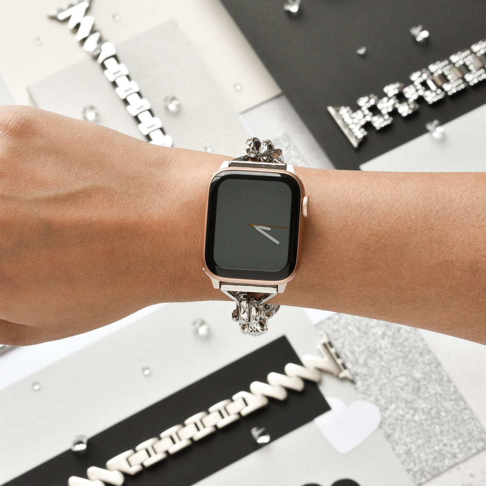 Close-up of the Chain Bracelet Apple Watch Strap - Silver by Coconut Lane on a person's wrist. The background features various stylish watch bands and metallic decorative elements, adding a sophisticated and modern aesthetic to the scene.