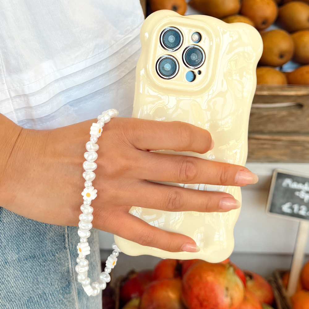 Girl next to fruit stand with phone case and Daisy Pearl phone strap attached