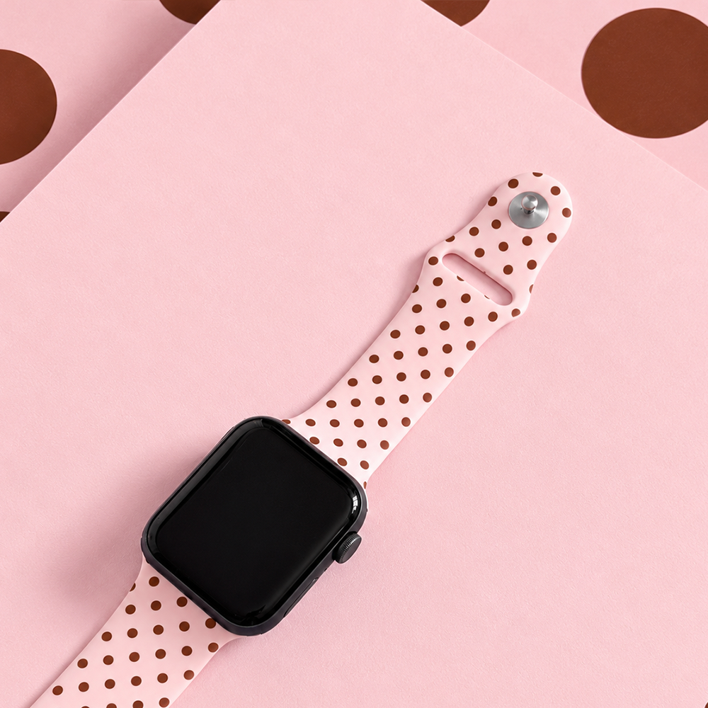 Pale pink silicone sport band with small brown polka dots, attached to a black Apple Watch smartwatch.