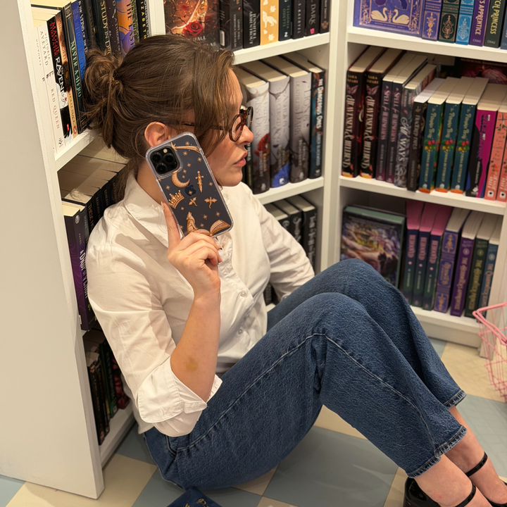 Woman holding an iphone with a clear fantasy girl phone case with golden illustrations of fantasy themed beaded effect icons, such as a book, wolf, crown, moon, sword, stars and dragons.
