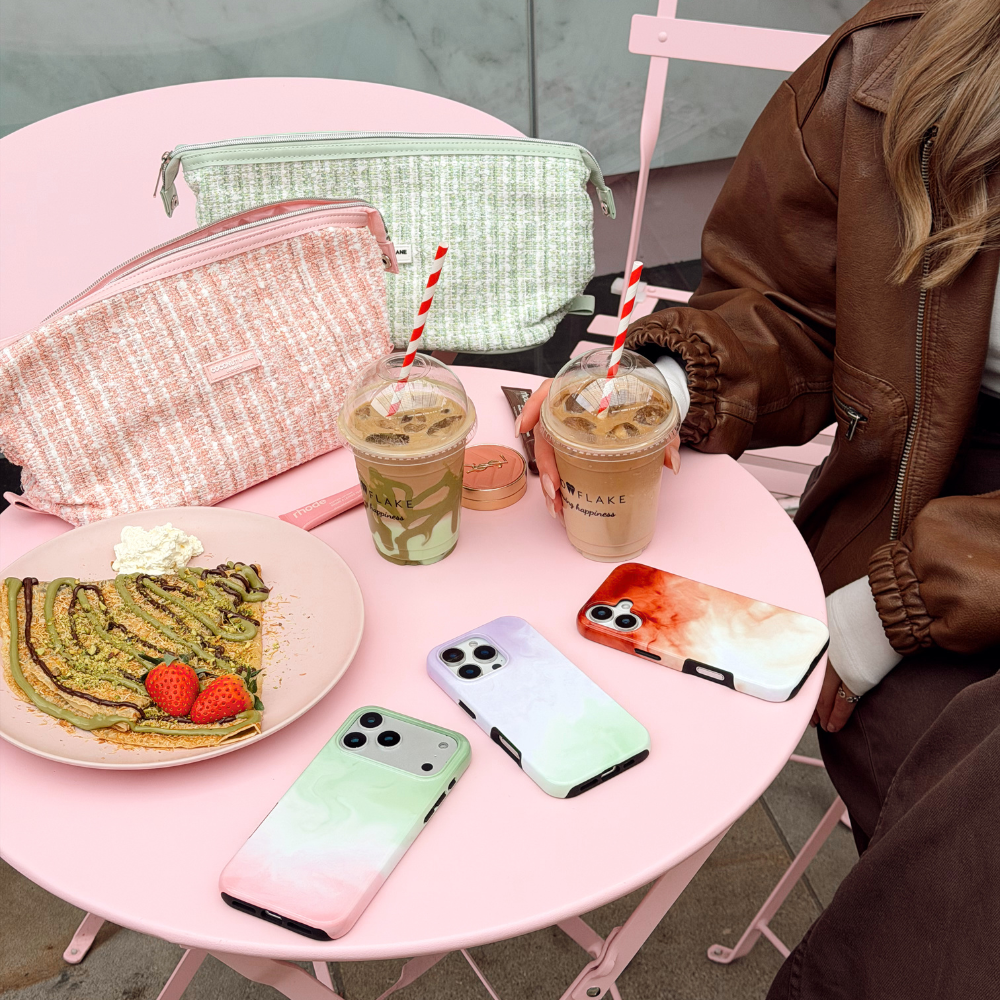 A flatlay in a cafe showcasing 2 matcha phone cases in strawberry and lavender and an iced latte phone case