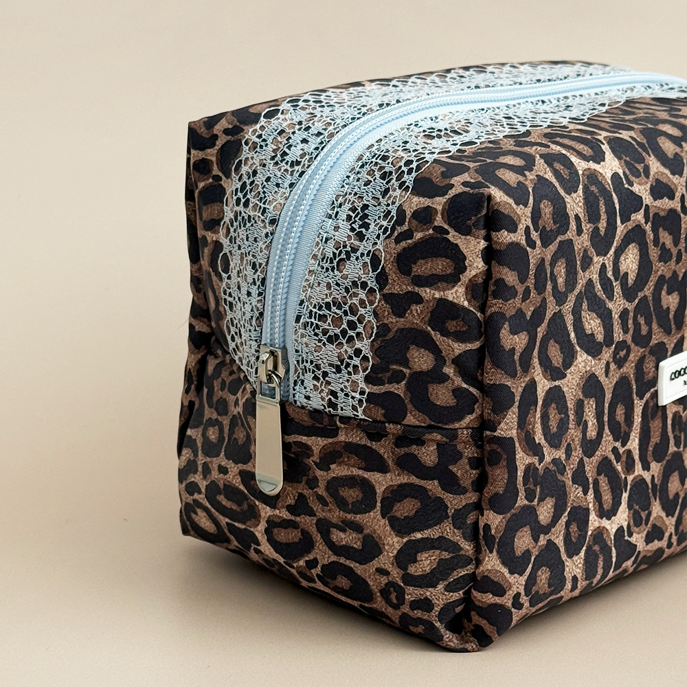 Close-up side view of Coconut Lane Leopard Lace makeup bag showing blue lace detailing, silver zip pull and brown leopard print fabric.