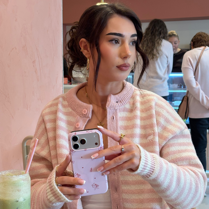 Girl in cafe wearing pink holding the Tough Phone Case in Love Notes