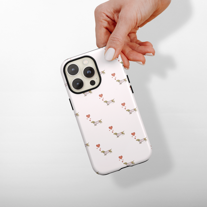Phone case with dachshund and heart pattern held by a hand on a white background