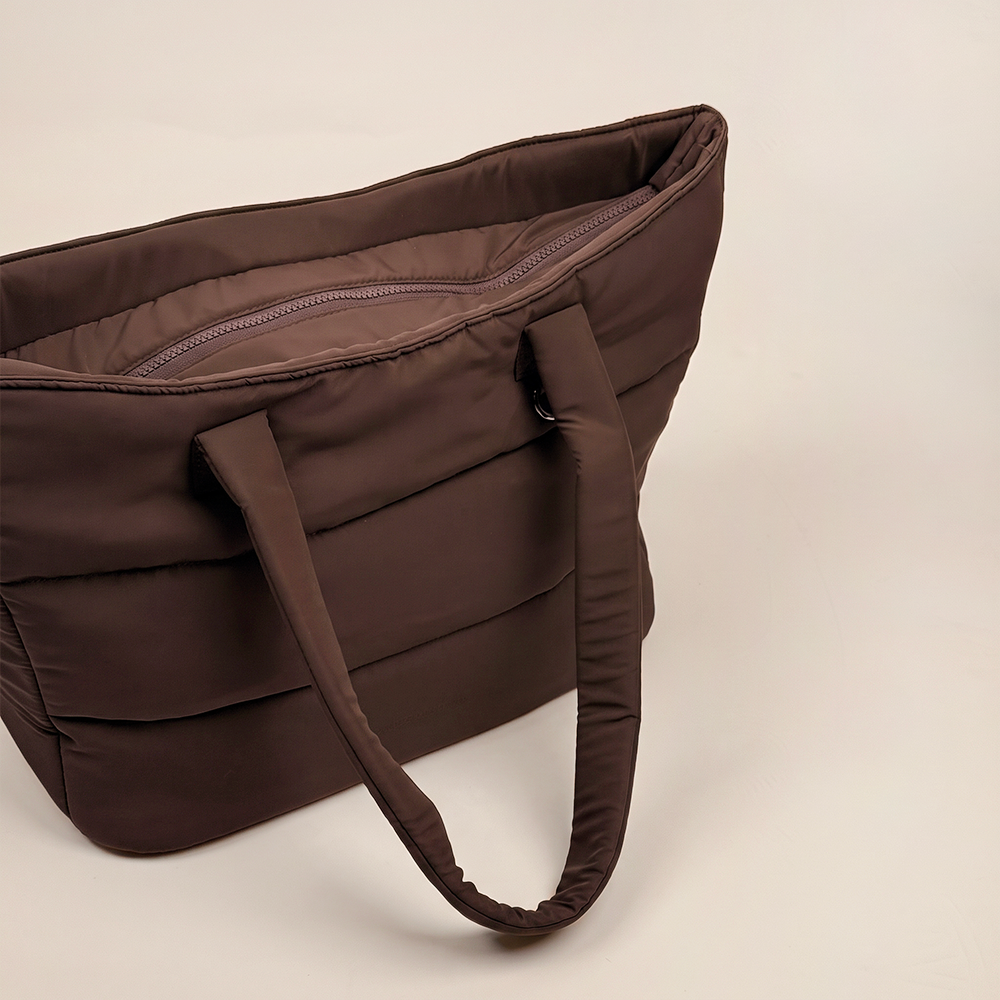 Angled close-up of the chocolate brown padded carryall bag, showing the open top, zip fastening, quilted fabric and shoulder straps.