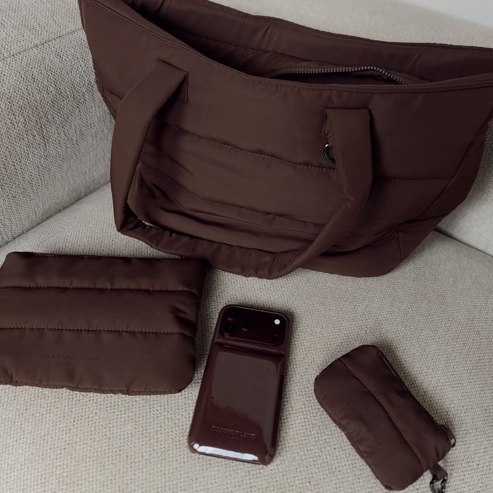 Chocolate brown padded puffer collection featuring a mini keyring bag with zip fastening, silver metal heart shaped clip, a Choc puffer everything pouch and the matching chocolate brown puffer phone case, all with the Coconut Lane logo. 