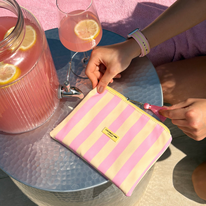 Person opening a pink and yellow striped pouch on a table with lemonade and a glass.
