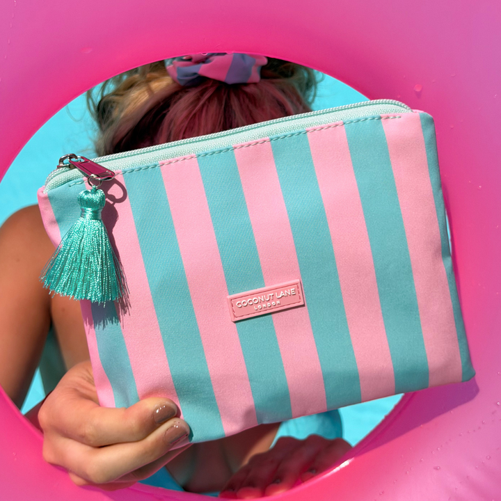 Pink and blue striped Mini Pouch with a tassel held by a person against a pink background