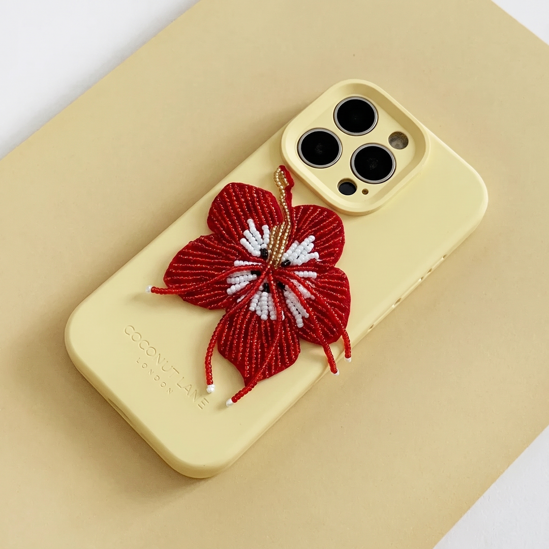 Red 3D hibiscus flower made from beads and sequins, on top of a yellow Coconut Lane Phone Case. 