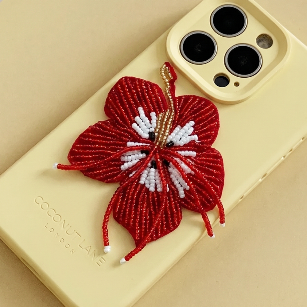 Red 3D hibiscus flower made from beads and sequins, on top of a yellow Coconut Lane Phone Case. 