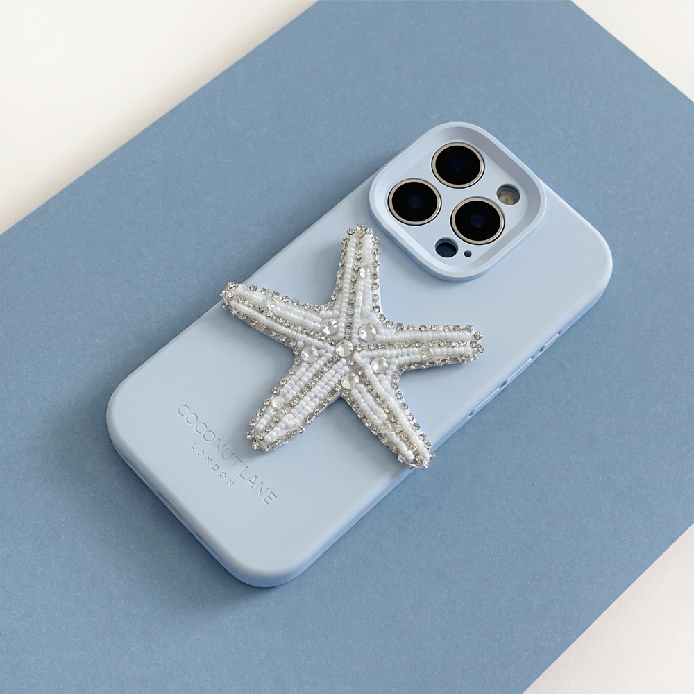 White and silver 3D starfish made from beads and sequins, on top of a blue Coconut Lane Phone Case. 