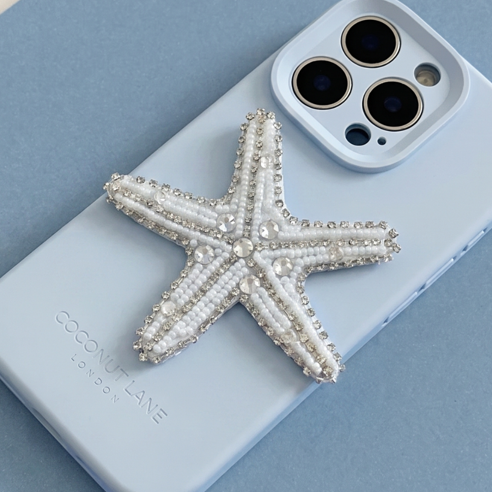 White and silver 3D starfish made from beads and sequins, on top of a blue Coconut Lane Phone Case. 