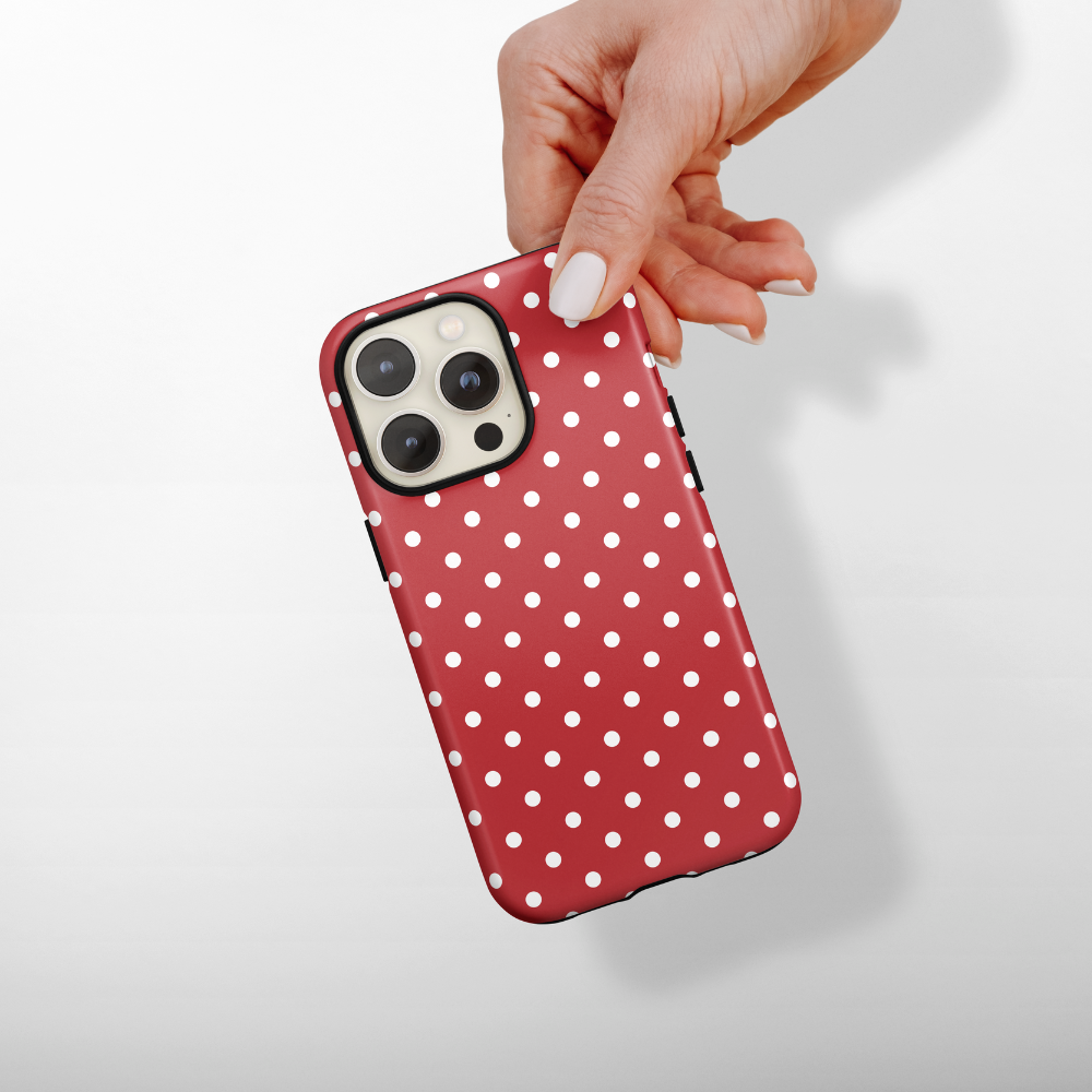 Hand holding a smartphone with a rouge polka dot Coconut Lane tough phone case against a plain background.