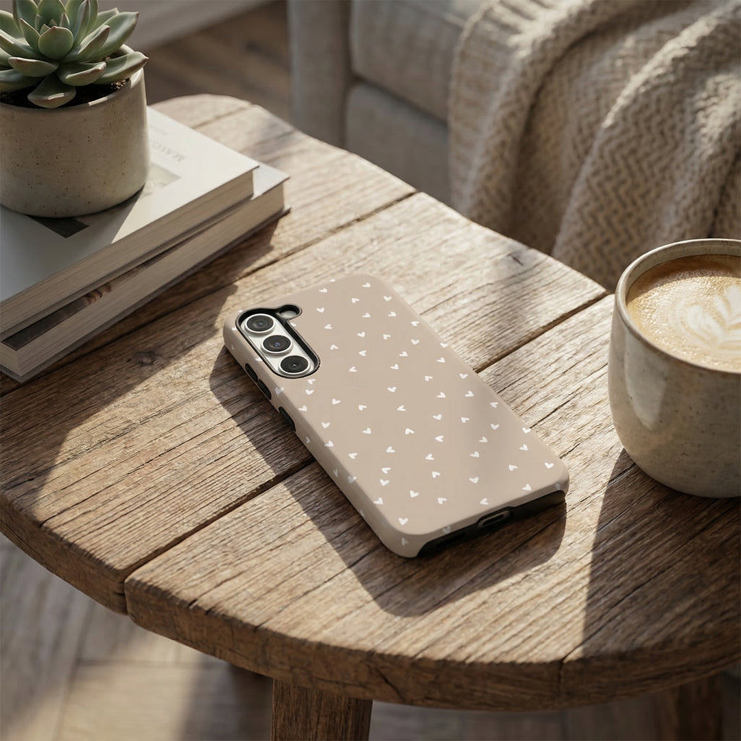 Phone case with white hearts on a wooden table with a cup of coffee and books.