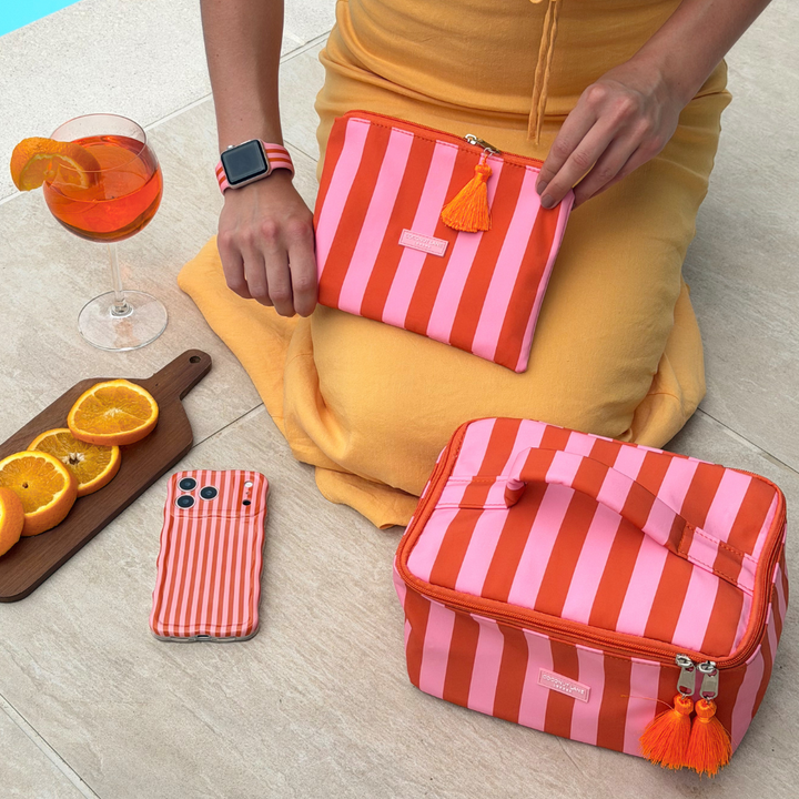 Person holding a pink and orange striped bag with another similar bag on the floor, next to a glass of orange juice and a phone.