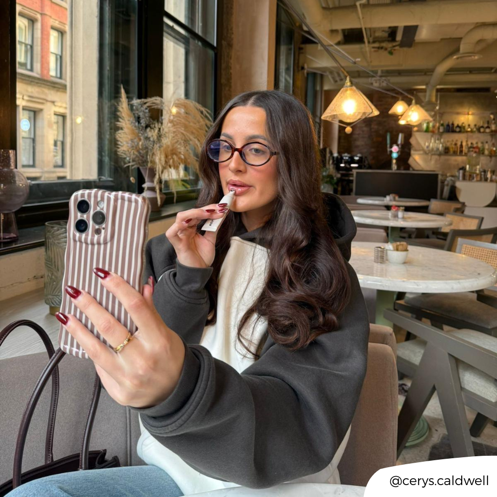Girl in cafe applying lip gloss holding wavy chestnut stripes phone case