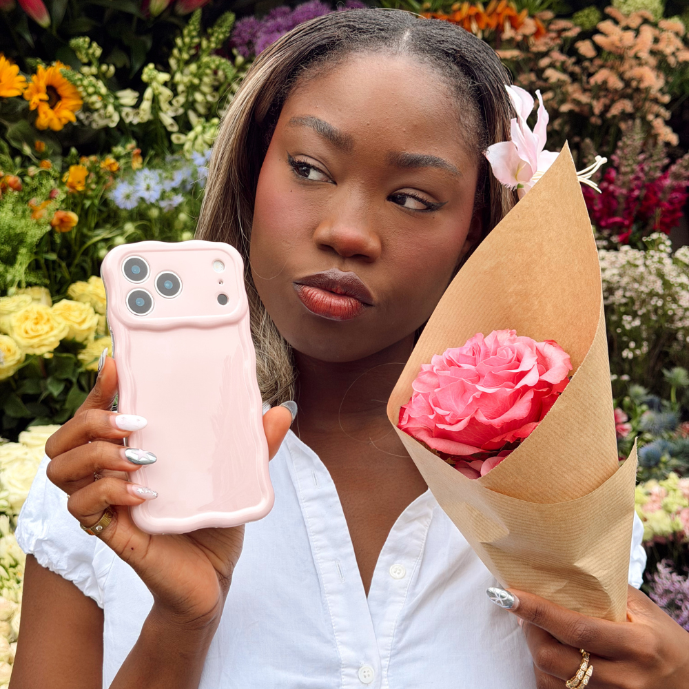 Girl by flower stand holding wavy pink phone case and flower