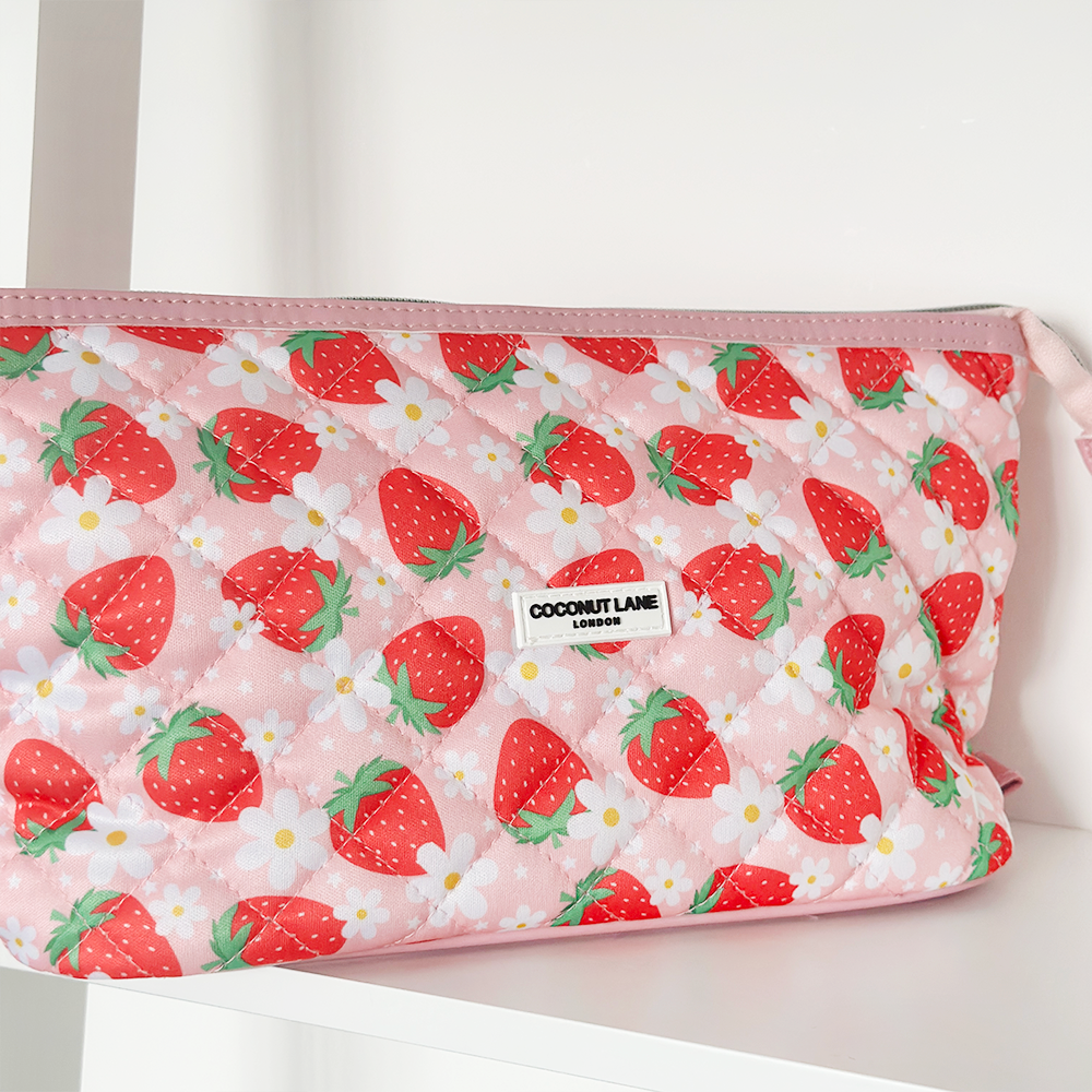 Quilted pink strawberry-print expandable makeup bag by Coconut Lane, displayed on a white shelf.