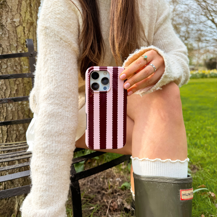 Girl sat in field with blushberry scallop stripes tough phone case in hand wearing cream outfit and wellies