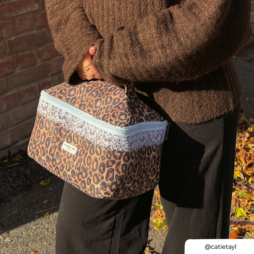 Woman in a brown knit jumper holding the Coconut Lane Leopard Lace vanity case featuring brown leopard print, pale blue lace trim.