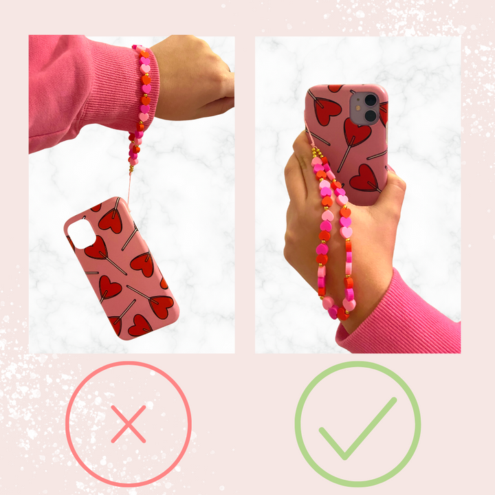 Two images side by side: The left image displays a phone case adorned with heart patterns, complemented by the "Beaded Phone Strap - Nude & Pearl" from Coconut Lane, which is dangling from a wrist. The right image features the same case being held with the "Beaded Phone Strap - Nude & Pearl" wrapped around the fingers. A red 'X' and green '✔' indicate incorrect and correct ways to hold the phone, respectively.