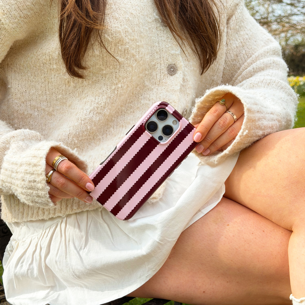Girl sat in field with blushberry scallop stripes tough phone case in hand wearing cream outfit
