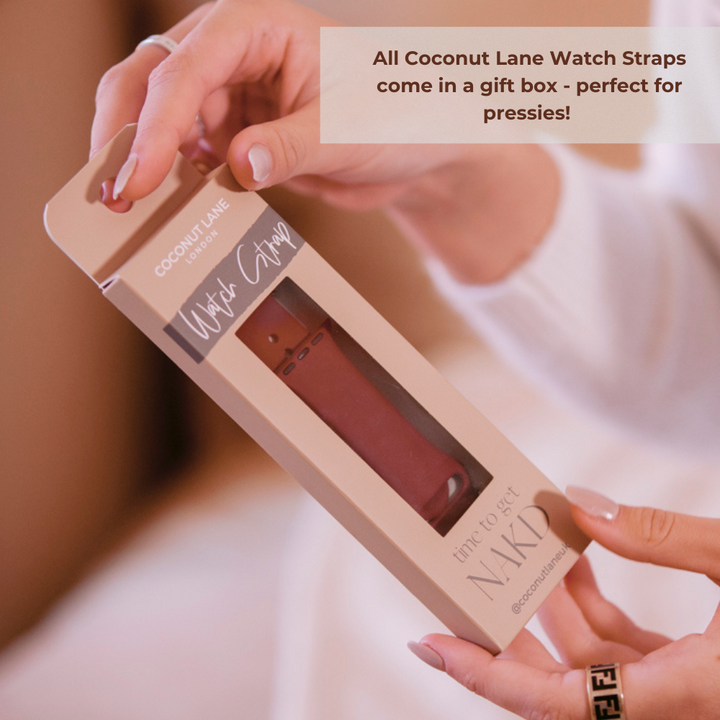 A person is holding a Coconut Lane Watch Strap gift box. The sleek, blush-colored box features a small window showcasing a Midnight Black silicone strap inside. Text on the image says, "All Coconut Lane Watch Straps come in a gift box - perfect for pressies!" Ideal for Apple Watch models.